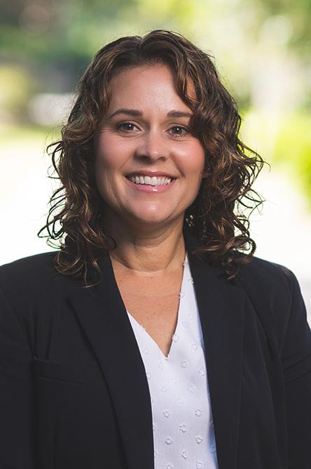 Lady standing outdoors in white blouse and black blazer smiling.